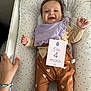 baby, infant, smiling, lying_down, cushion, clothing, bib, hand, milestone_card, heart_pattern, bed, person, cute, happy, indoors, fabric, skin, face, child, four_months