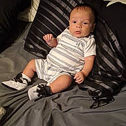Ryatt is registered to the contest to win money with this photo: baby, bed, black_and_white_shoes, blanket, casual_wear, child, curious, cute, furniture, indoors, infant, person, pillow, portrait, resting, romper, shoes, striped_clothing, striped_pillow, young_child