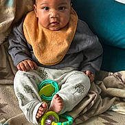 Nadir is registered to the contest to win money with this photo: baby, child, infant, bib, toy, blanket, couch, feet, hands, clothing, pattern, face, cute, sitting, indoors, curious, young, comfort, colorful, expression