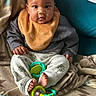 baby, child, infant, bib, toy, blanket, couch, feet, hands, clothing, pattern, face, cute, sitting, indoors, curious, young, comfort, colorful, expression