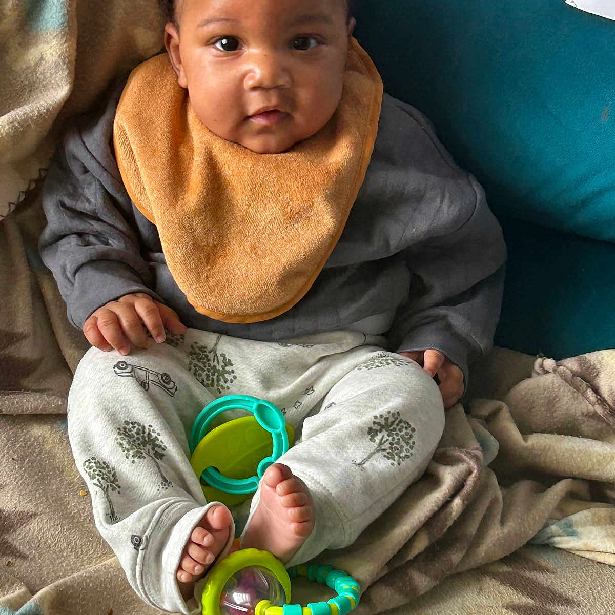 Nadir is registered to the contest to win money with this photo: baby, child, infant, bib, toy, blanket, couch, feet, hands, clothing, pattern, face, cute, sitting, indoors, curious, young, comfort, colorful, expression
