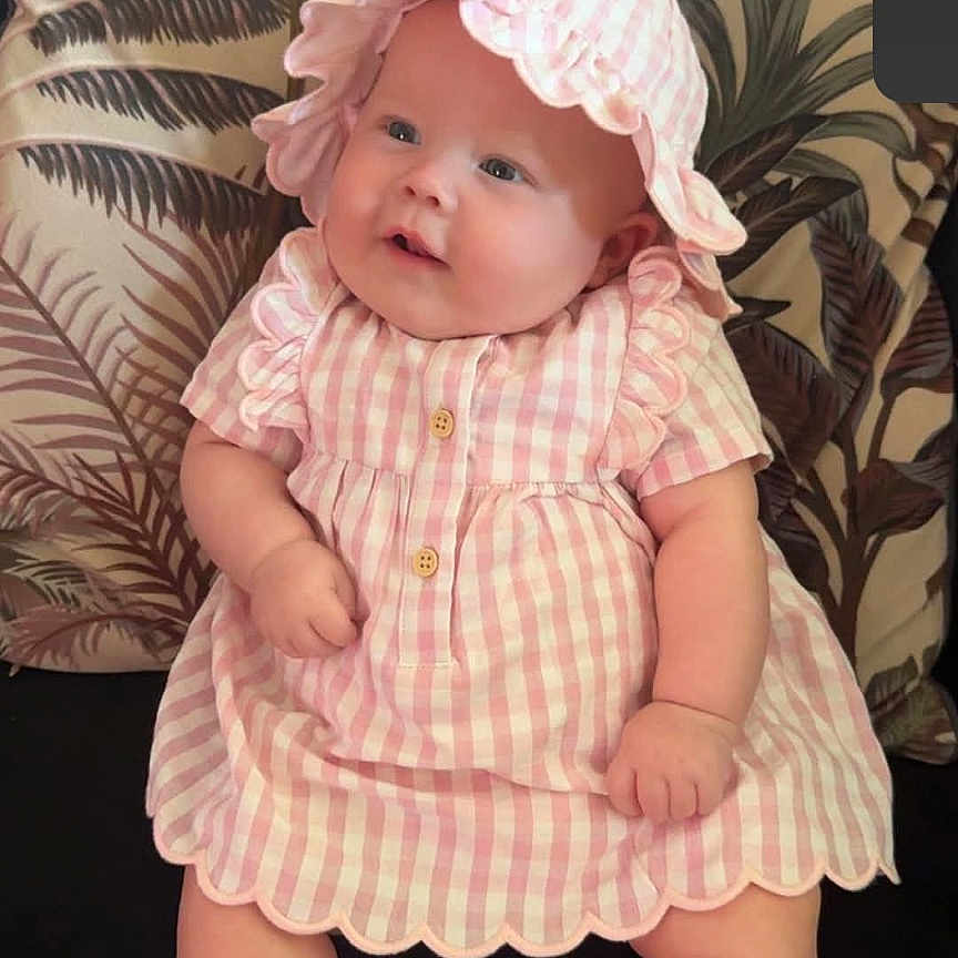 Lily-Jo is registered to the contest to win money with this photo: baby, bonnet, cap, clothing, costume, cushion, dress, face, footwear, hat, head, homedecor, hosiery, newborn, person, photography, portrait, shoe, sitting, sock