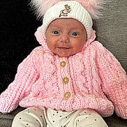 Paisley joined the competition — help win amazing prizes! baby, smiling, pink_sweater, knitted_clothing, white_hat, pom_poms, blue_eyes, polka_dot_pants, infant, cute, cozy, seated, couch, indoor, portrait, child, happy, warm_clothing, headwear, small_person