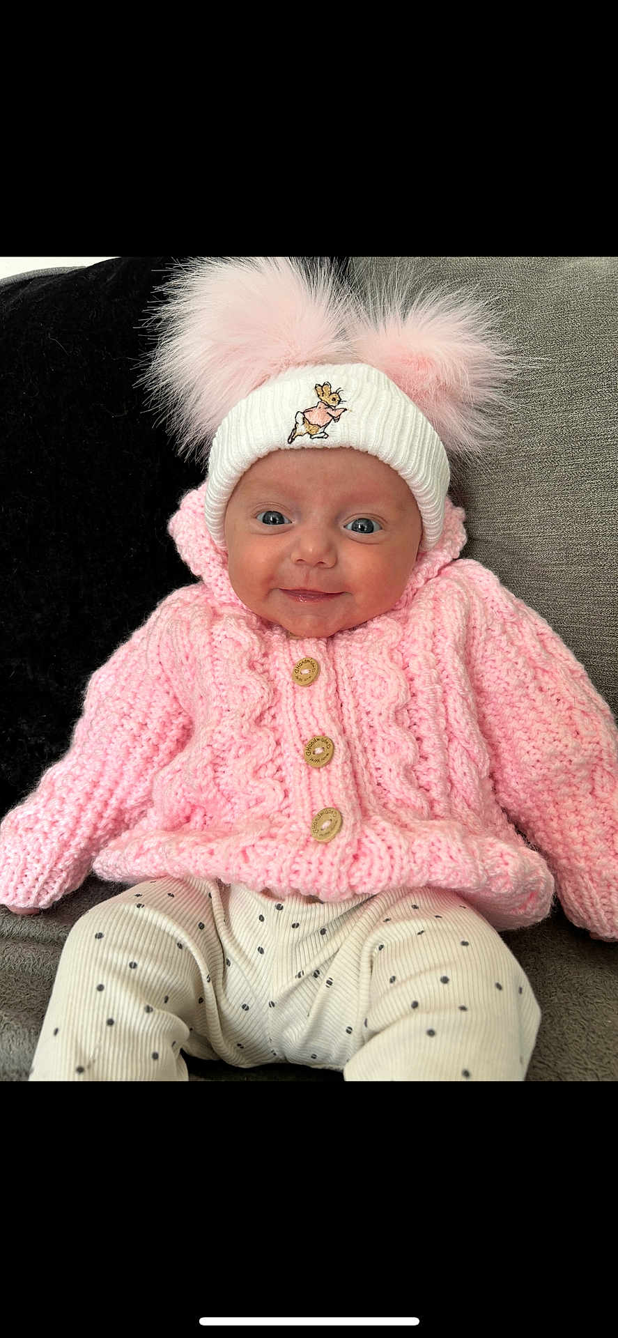Paisley joined the competition — help win amazing prizes! baby, smiling, pink_sweater, knitted_clothing, white_hat, pom_poms, blue_eyes, polka_dot_pants, infant, cute, cozy, seated, couch, indoor, portrait, child, happy, warm_clothing, headwear, small_person
