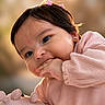 baby, child, infant, girl, pink_clothing, toy, hand, hair_clips, earrings, cute, chewing, portrait, close_up, warm_light, soft_toy, happy, smiling, outdoor, blurry_background, young
