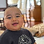 baby, blurred_background, child, clothing, cute, dark_shirt, face, happy, head, home, indoor, infant, moon, mountain, pattern, person, portrait, seated, smiling, warm_lighting