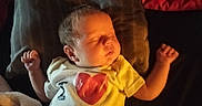 Sophia is registered to the contest to win money with this photo: baby, blanket, closed_eyes, cozy, cushion, dad_shirt, family, furniture, heart, indoors, infant, newborn, onesie, pillow, portrait, raised_fists, relaxed, sleeping, warm_lighting, yellow_outfit