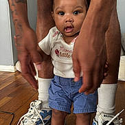 Noemi joined the competition — help win amazing prizes! toddler, child, baby, red_bow, shorts, white_shirt, red_sandals, socks, sneakers, tattoo, legs, floor, indoor, person, hands, wooden_floor, curious, standing, casual_clothing, portrait