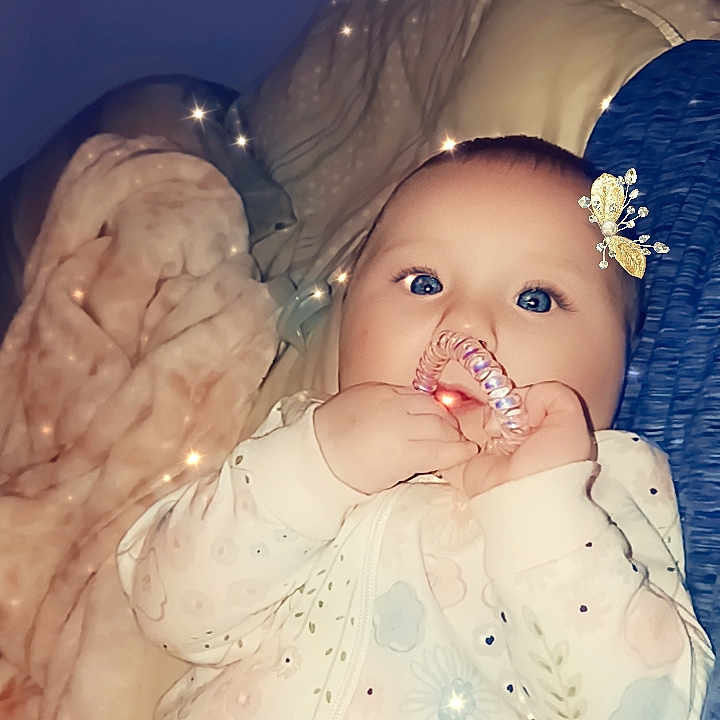 Aurora is registered to the contest to win money with this photo: baby, blanket, bodypart, clothing, couch, dress, eating, face, finger, furniture, hand, happy, hat, head, mouth, newborn, person, photography, portrait, smile