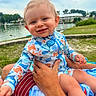 baby, child, smile, swimsuit, ocean_theme, water, lake, outdoor, grass, adult_hand, person, nature, cloudy_sky, greenery, portrait, happy, summer, vacation, holding, playful