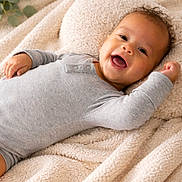 Zaya joined the competition — help win amazing prizes! baby, smiling, infant, blanket, cozy, onesie, happy, cute, portrait, child, lying_down, soft, warm, curly_hair, skin, face, indoors, comfort, relaxed, expression