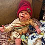 Arthur joined the competition — help win amazing prizes! baby, child, beanie, red_hat, couch, blanket, toy, patterned_cushion, smiling, reaching_hand, indoor, soft_toys, comfortable, casual_clothing, infant, happy, cute, cozy, playful, portrait