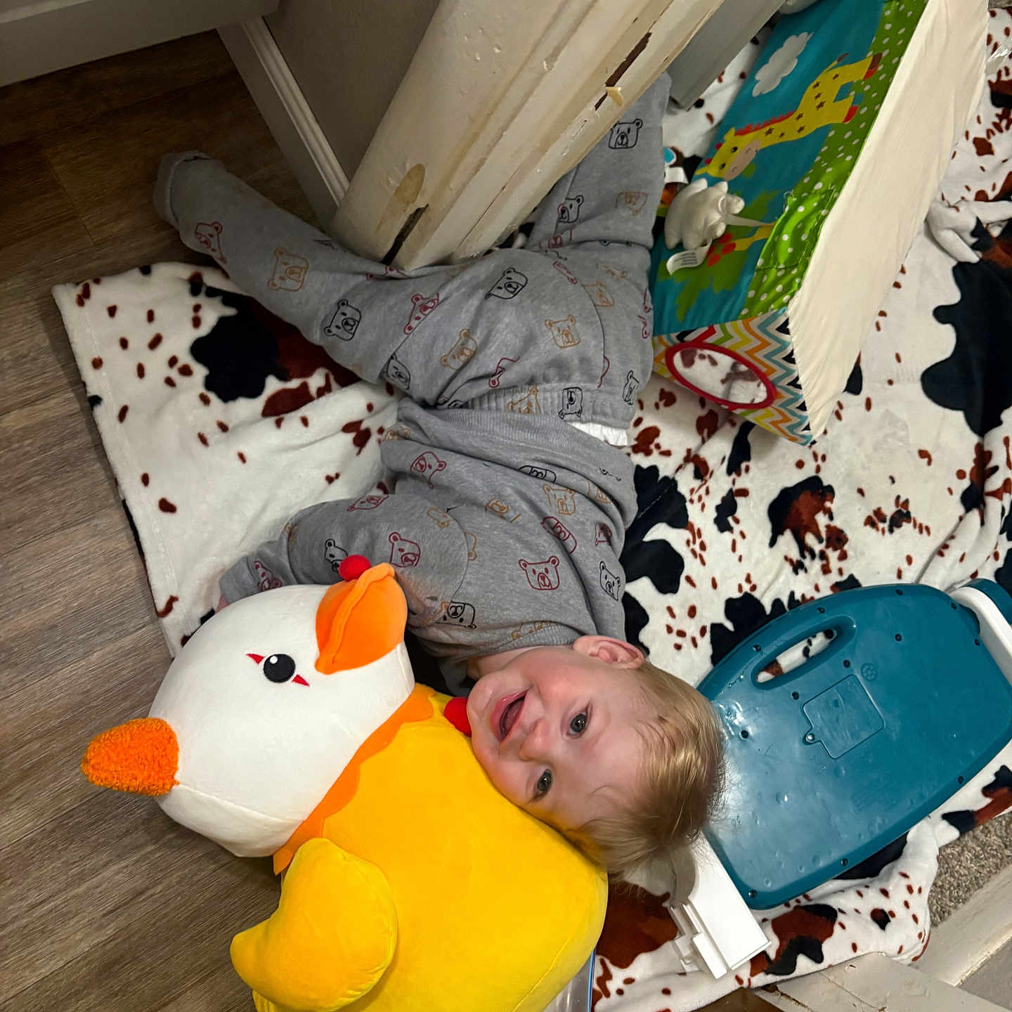 Arthur is registered to the contest to win money with this photo: blanket, child, colorful, cozy, cute, duck, face, floor, happy, head, home, indoor, lamp, pajamas, playtime, plush_toy, smiling, toddler, toy, wood_floor