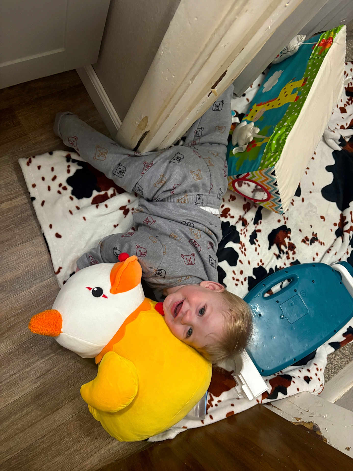 Arthur is registered to the contest to win money with this photo: toddler, child, plush_toy, duck, pajamas, blanket, floor, lamp, indoor, smiling, happy, toy, playtime, face, head, wood_floor, colorful, cozy, cute, home