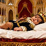 baby, bed, child, costume, crown, decor, gold, indoor, infant, laying_down, luxury, palace, portrait, regal, rich, royalty, smile, soft_pillow, throne_room, velvet