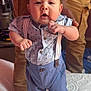 Konrad is registered to the contest to win money with this photo: baby, child, person, shirt, suspenders, tattoo, hand, foot, bed, mattress, pattern, blue, skin, clothing, indoor, standing, curious, expression, adult, support