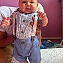 baby, child, person, suspenders, blue_shorts, floral_shirt, indoor, bed, purple_wall, hand, smiling, cute, feet, portrait, infant, clothing, furniture, adult_hand, happy, standing