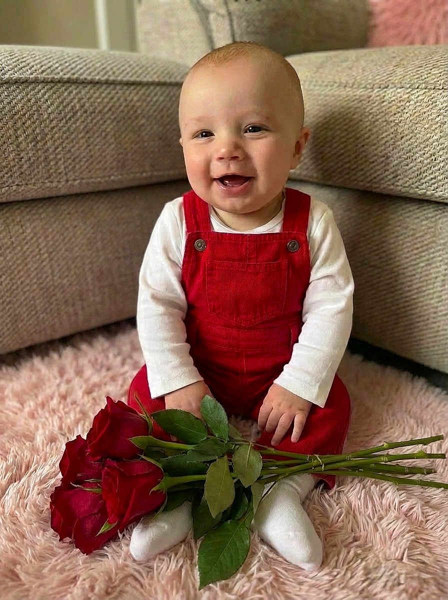 Cory-Grey joined the competition — help win amazing prizes! baby, infant, smiling, red_overalls, white_shirt, roses, bouquet, plush_rug, sitting, couch, living_room, portrait, indoor, happy, hands, socks, closeup, face, toddler, valentines