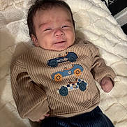 Ezra is registered to the contest to win money with this photo: baby, infant, sweater, clothing, car_patches, blanket, bed, smiling, face, person, cute, cozy, indoor, child, young, portrait, knitwear, happy, resting, soft
