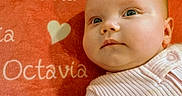 Octavia is registered to the contest to win money with this photo: baby, infant, face, portrait, closeup, child, blanket, heart, text, name, pink, clothing, soft_texture, cute, skin, person, young, lying_down, expression, indoor