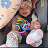 baby, smiling, car_seat, toy, blanket, headband, clothing, infant, happy, cute, child, seatbelt, pink, floral, indoors, portrait, person, footwear, bottle, colorful