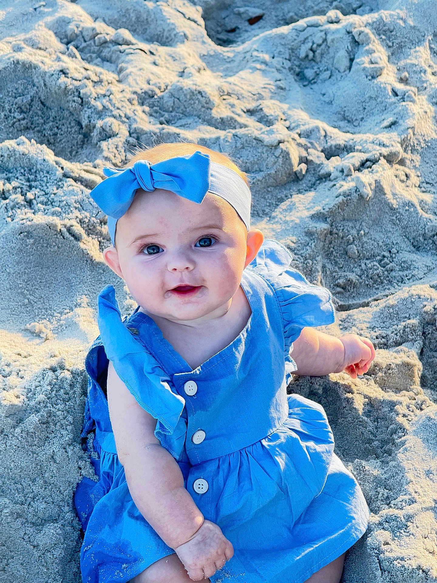 Claire joined the competition — help win amazing prizes! baby, child, blue_dress, headband, bow, sand, beach, smile, face, cute, sunlight, outdoor, sitting, happy, infant, person, skin, eyes, portrait, summer