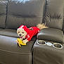dog, puppy, hoodie, red_hoodie, couch, leather_sofa, plush_toy, banana_toy, tongue_out, pet, indoor, living_room, curtains, window_light, cup_holders, stitching, armrest, small_dog, playful, adorable