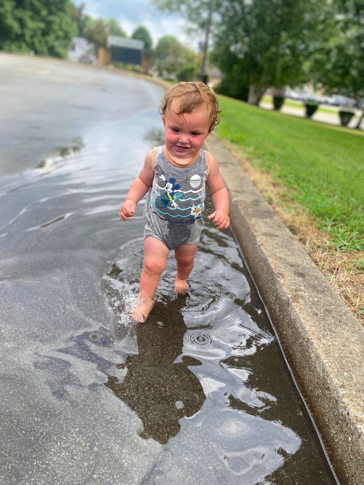 Barrett is registered to the contest to win money with this photo: asphalt, body_of_water, child, fun, grass, happy, joy, leg, leisure, people_in_nature, person, plant, puddle, recreation, road, road_surface, sky, smile, toddler, tree