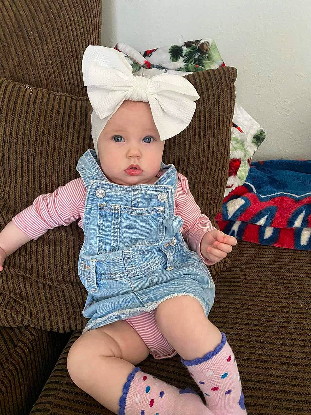 Emberly is registered to the contest to win money with this photo: baby, baby_toddler_clothing, child, couch, dress, fashion_accessory, headband, headgear, headwear, human_leg, jewellery, lap, leg, pattern, person, pink, sitting, sleeve, sock, thigh
