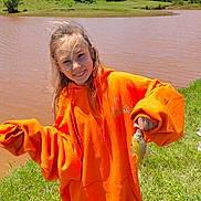 Madalynn is registered to the contest to win money with this photo: child, girl, fish, fishing, hoodie, orange_clothing, outdoor, pond, water, grass, smile, happy, nature, sunlight, portrait, casual, wind, small_fish, recreation, daytime