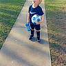 child, boy, soccer_ball, water_bottle, sidewalk, grass, sunlight, visor, sportswear, shorts, socks, shoes, smiling, outdoor, daylight, recreation, happy, playing, leisure, neighborhood