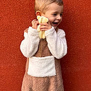 Célyan participe au concours pour gagner de l'argent avec cette photo : child, toddler, plush_toy, brown_outfit, white_pocket, smiling, happy, fuzzy_clothing, cute, portrait, standing, holding, toy, background, wall, texture, short_hair, playful, joyful, outdoor