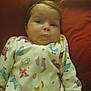 Mallory is registered to the contest to win money with this photo: baby, infant, onesie, dinosaur_print, red_cushion, lying_down, cute, pout, expression, child, soft_lighting, indoors, sleepwear, hand, face, head, person, young_child, skin, hair