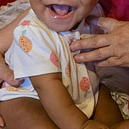 Saïan participe au concours pour gagner de l'argent avec cette photo : baby, smiling, infant, child, onesie, fruit_pattern, hand, pillow, happy, cute, sitting, indoors, person, skin, face, mouth_open, toes, support, closeup, joyful