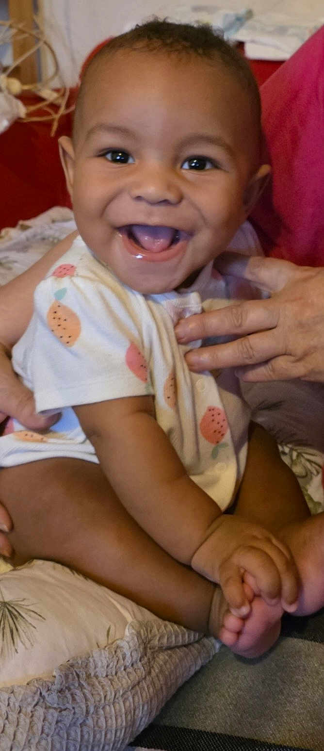 Saïan participe au concours pour gagner de l'argent avec cette photo : baby, smiling, infant, child, onesie, fruit_pattern, hand, pillow, happy, cute, sitting, indoors, person, skin, face, mouth_open, toes, support, closeup, joyful