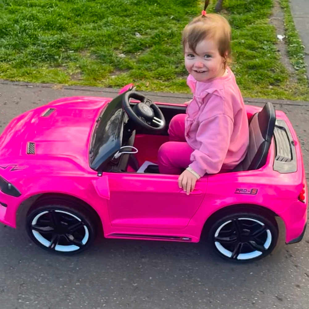 Aria is registered to the contest to win money with this photo: alloywheel, car, carwheel, child, face, grass, head, machine, nature, outdoors, park, person, photography, plant, portrait, spoke, tire, transportation, vehicle, wheel
