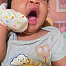 baby, yawning, mitten, clothing, grey_shirt, sun_graphic, skateboard, nursery, pastel_colors, indoor, child, cute, adorable, infant, portrait, happy, sleepy, person, room, decor