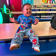 Asahd is registered to the contest to win money with this photo: child, toddler, smiling, laughing, indoor, table, bench, clothing, spiderman, jeans, tshirt, shoes, colorful, playful, decor, lighting, bag, happy, portrait, person