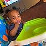 baby, infant, high_chair, smile, living_room, television, cartoon, tray, polka_dot, christmas_tree, earrings, hair_buns, cute, happy, portrait, furniture, toy, child, playful, feeding