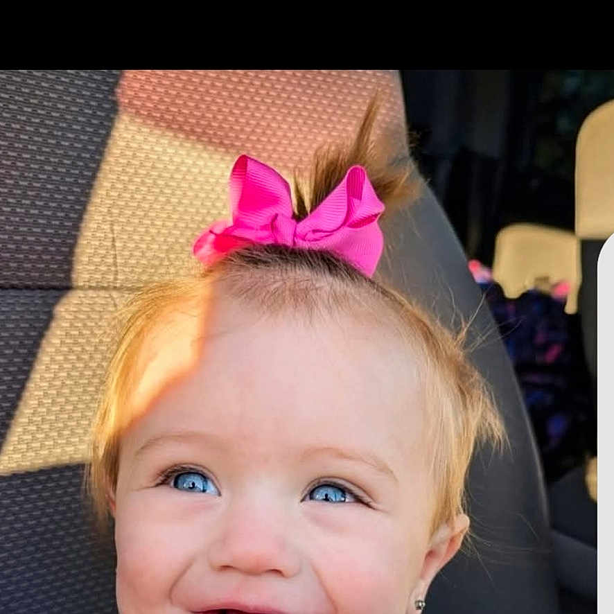 Morti is registered to the contest to win money with this photo: baby, blue_eyes, car_seat, cheeks, child, close_up, eyelashes, hair_bow, happy, head, passenger, pink_bow, playful, portrait, seat, shadow, smile, sunlight, toddler, vehicle_interior