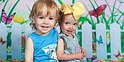 Jesse joined the competition — help win amazing prizes! background, black_crocs, blue_clothing, butterfly, child, cute, flower, green_floor, happy, indoor, pink_crocs, playful, portrait, sitting, smile, studio_photo, toddler, white_picket_fence, wooden_crate, yellow_bow