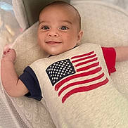 Jonathan is registered to the contest to win money with this photo: baby, infant, smile, face, eyes, crib, mesh, clothing, american_flag, red, blue, white, pattern, person, cute, lying_down, indoors, portrait, child, happy