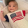 baby, infant, smile, face, eyes, crib, mesh, clothing, american_flag, red, blue, white, pattern, person, cute, lying_down, indoors, portrait, child, happy
