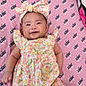 baby, infant, smiling, floral_dress, headband, pink_blanket, juicy_logo, cute, lying_down, happy, child, portrait, apparel, patterned_clothing, one_person, indoors, closeup, skin, baby_girl, small_child