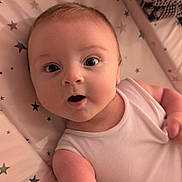 Ezra is registered to the contest to win money with this photo: baby, infant, child, onesie, pink, star_pattern, cushion, blanket, reaching, curious, face, eyes, skin, arm, indoor, closeup, person, young, expression, soft_lighting