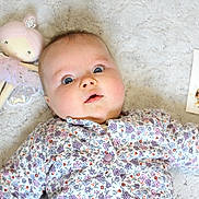 Louise a rejoint le concours — aidez-le/la à gagner de superbes lots ! baby, infant, floral_clothing, blanket, soft_texture, doll, fairy_doll, milestone_card, portrait, cute, child, blue_eyes, laying_down, indoors, closeup, face, expression, young_child, adorable, baby_girl