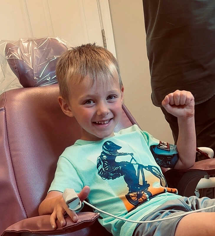 Enverson joined the competition — help win amazing prizes! child, boy, smiling, chair, tshirt, bmx, medical_device, finger_sensor, shorts, indoor, happy, person, casual_clothing, young, light_skin, short_hair, seated, healthcare, hospital, raising_fist