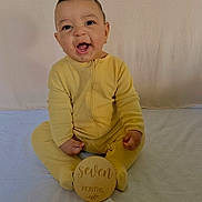 Roman is registered to the contest to win money with this photo: baby, infant, yellow_onesie, smiling, sitting, milestone, wooden_sign, seven_months, blanket, cute, portrait, child, happy, indoors, young_child, person, face, head, one_person, clothing