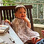 toddler, child, smiling, table, wooden_chair, blanket, outdoor, railing, greenery, face, baby, food, spoon, foil, hand, foot, clothing, happy, dining, person