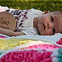 baby, infant, blanket, crochet, outdoor, grass, wooden_plaque, two_months, clothing, person, face, head, skin, hand, lying_down, colorful, soft_texture, young_child, cute, portrait